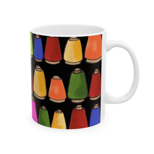 White mug with colorful thread spools pattern on a black background.